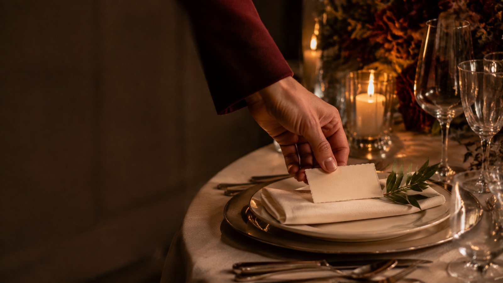 A hand placing a calligraphed place card on a folded napkin at a candlelit table — studio concept imagery.